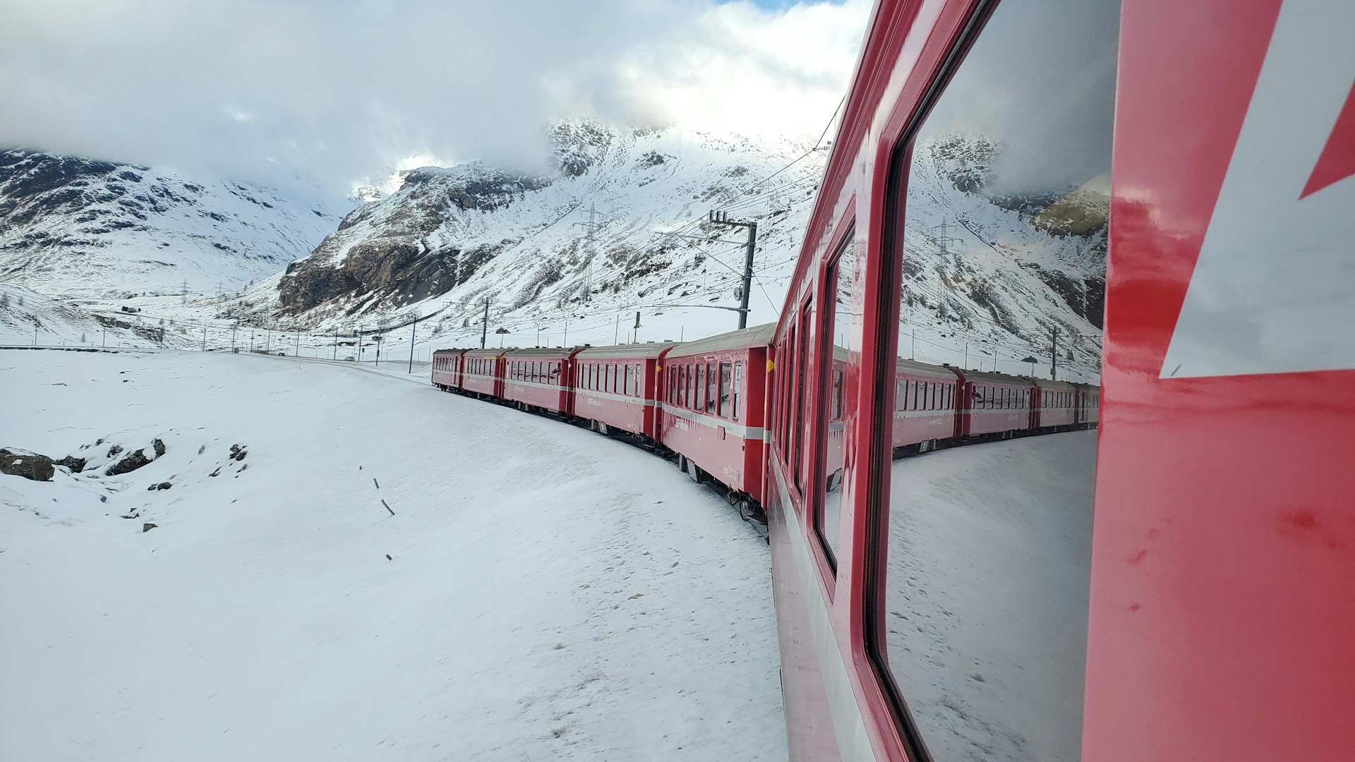 Red passenger train curving through a snowy Alpine mountain landscape viewed from inside the train window in winter