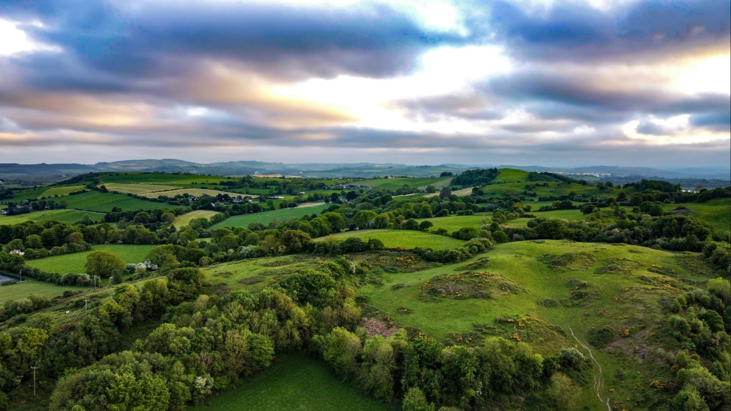 Aerial view of rolling green hills and countryside in County Cork, Ireland, under a dramatic cloudy sky