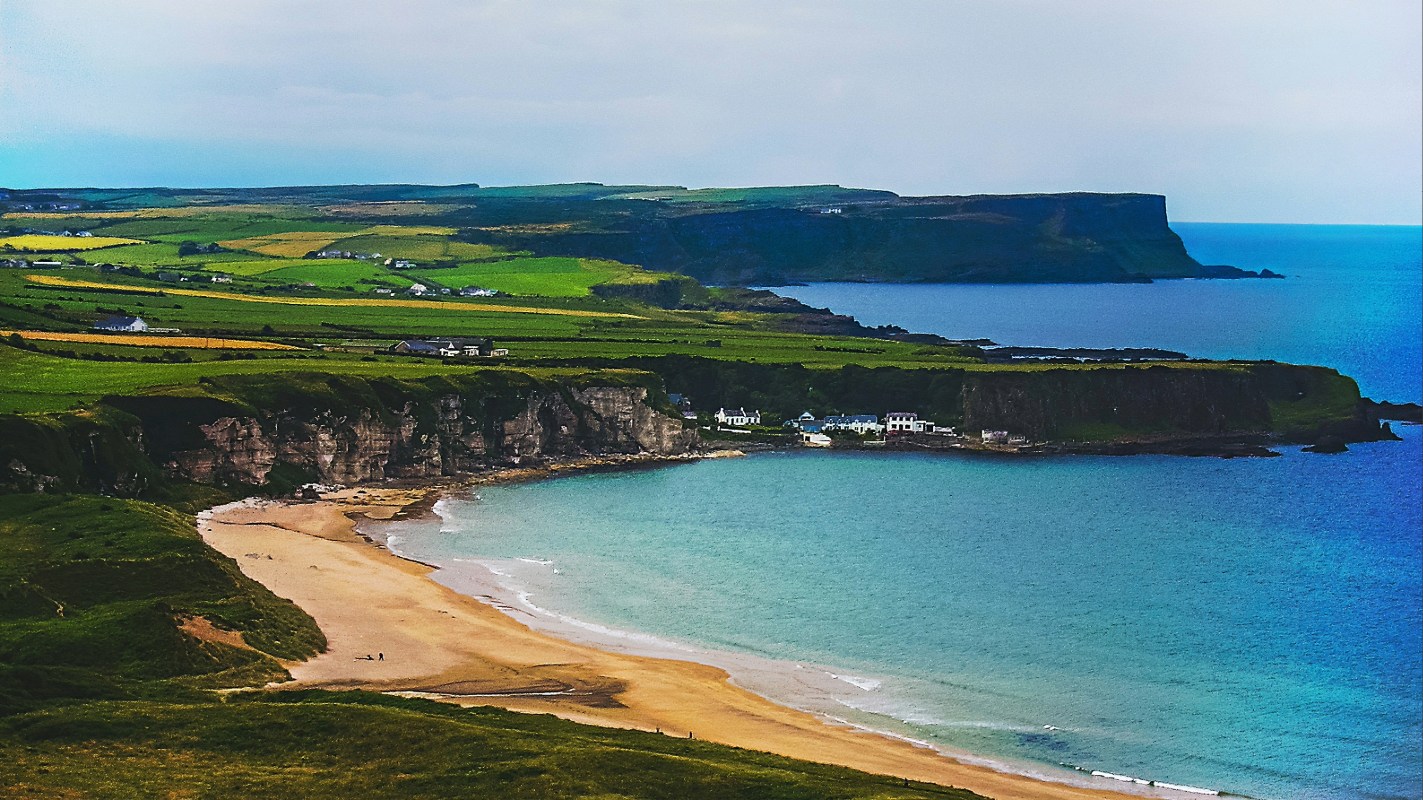 Aerial view of a sandy beach cove with turquoise water and green coastal cliffs along Ireland's Wild Atlantic Way
