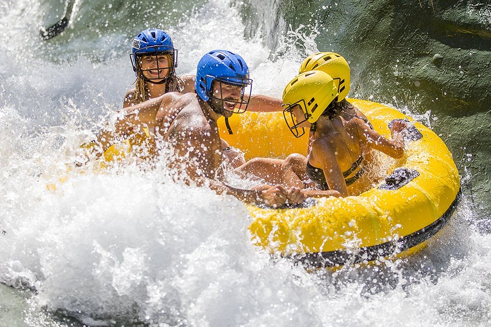 Three people wearing helmets riding a yellow inflatable tube through a white water splash ride at a water park