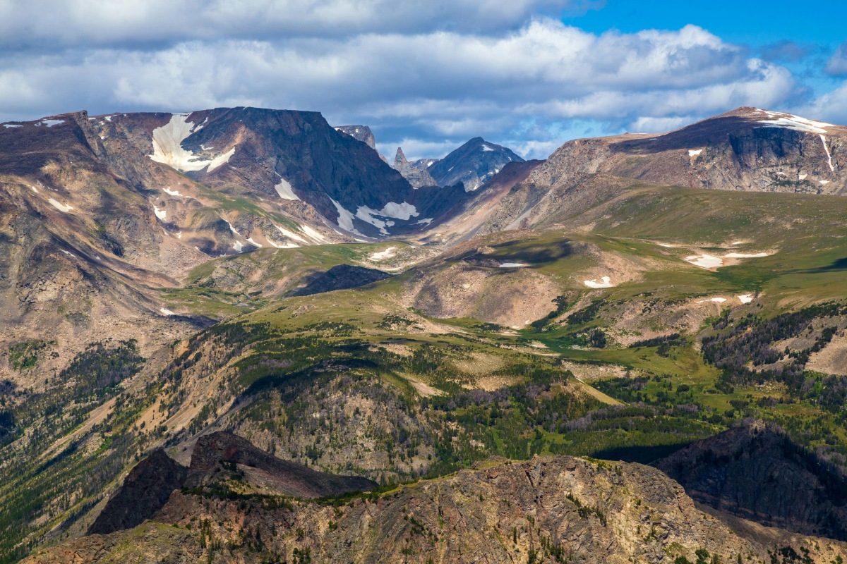Panoramic view of the Beartooth Mountains alpine landscape with rocky peaks, snow patches, and green valleys near the Beartooth Highway, Montana