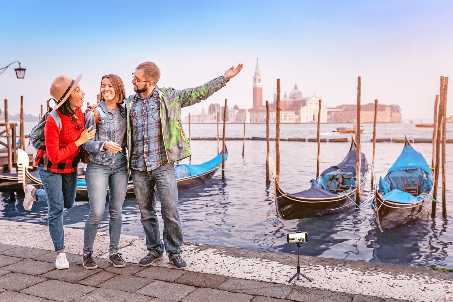 Group of happy friends travelers having fun on San Marco Square with gondolas and Grand channel at the background in Venice. Vacation and holidays in Italy and Europe concept