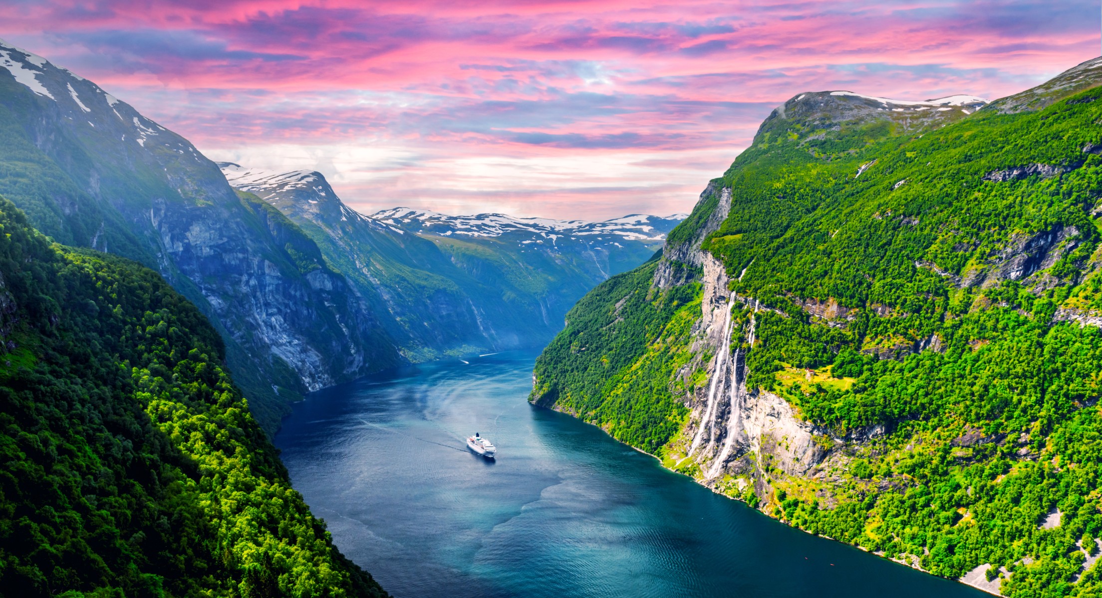 Cruise ship sailing through Norway’s Geirangerfjord surrounded by mountains and waterfalls