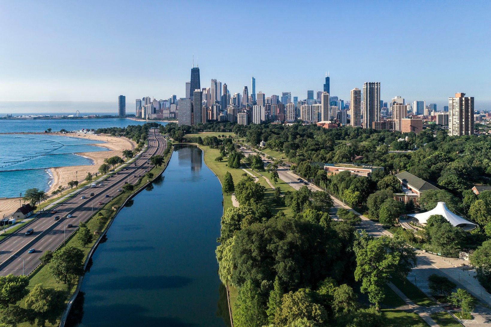 Aerial view of Chicago lakefront showing Lincoln Park green space, Lake Shore Drive, Lake Michigan beach, and downtown skyline on a clear summer day