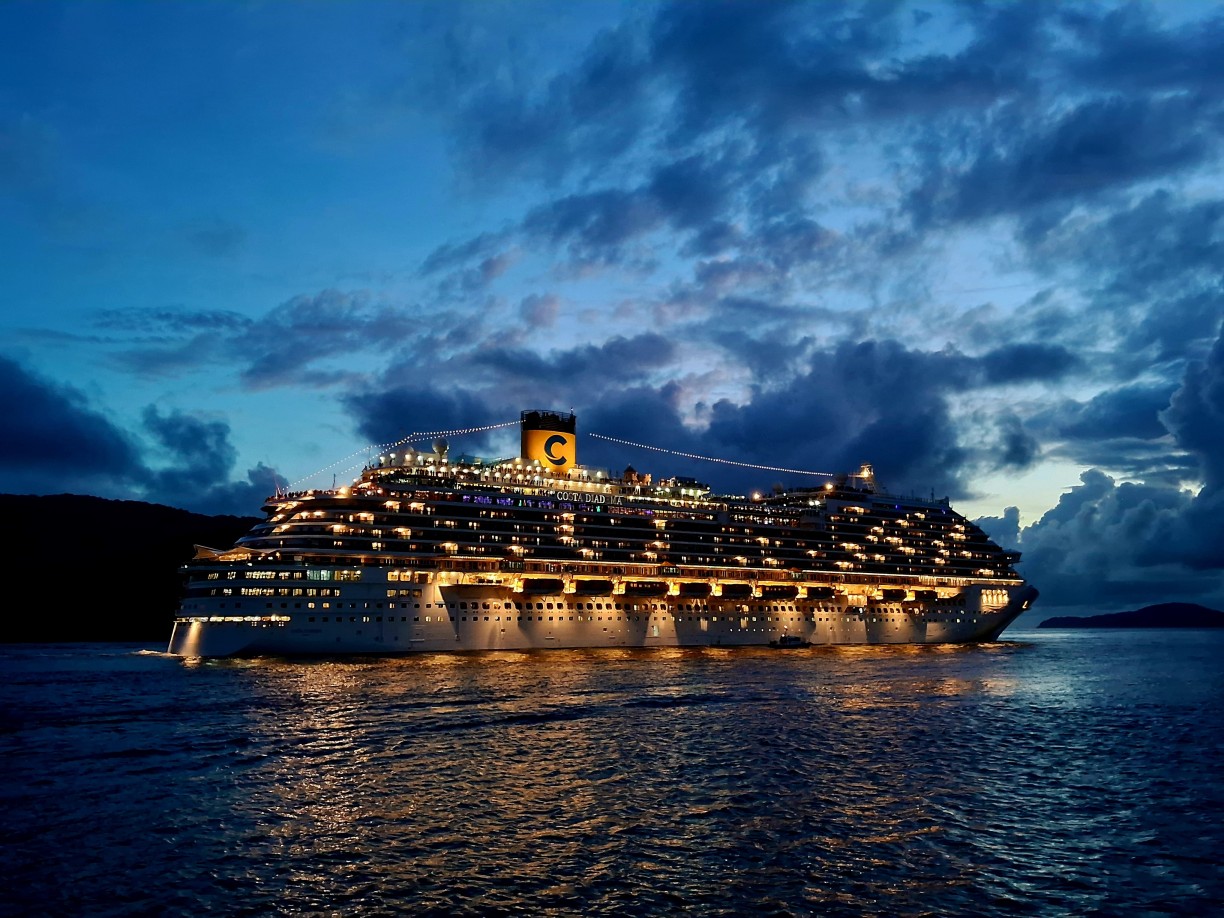 Large illuminated cruise ship with yellow funnel sailing at night under dramatic blue storm clouds on open ocean