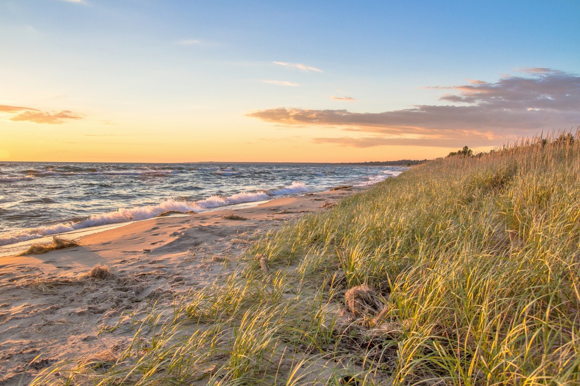 Summer Beach Background. Remote beach bathed in golden light with sand dunes and dune grass. St. Ignace, Michigan.
