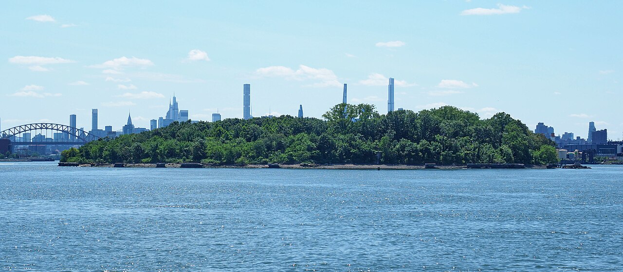 North Brother Island seen from Barretto Point Park, Bronx, New York. Hell Gate Bridge visible at left edge of frame. Manhattan skyline in the background.