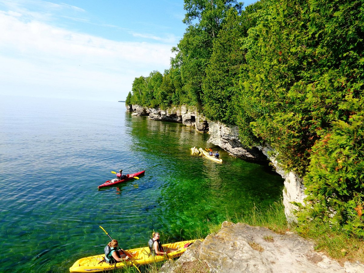 Kayakers paddling on clear green water along white limestone cliffs and green trees at Door County Wisconsin on a summer day