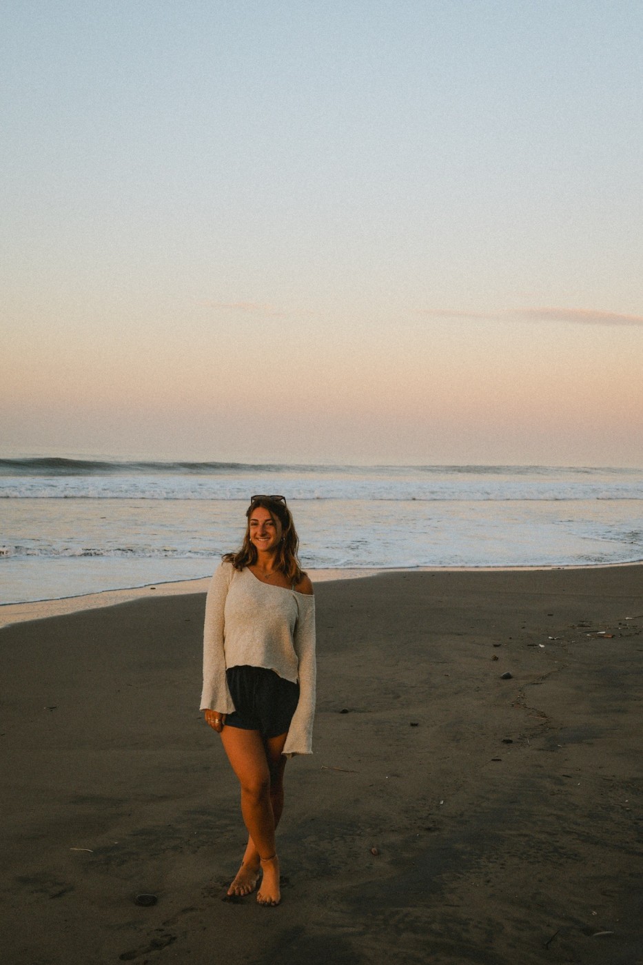 Traveler walking barefoot on a beach at sunset during long-term travel.