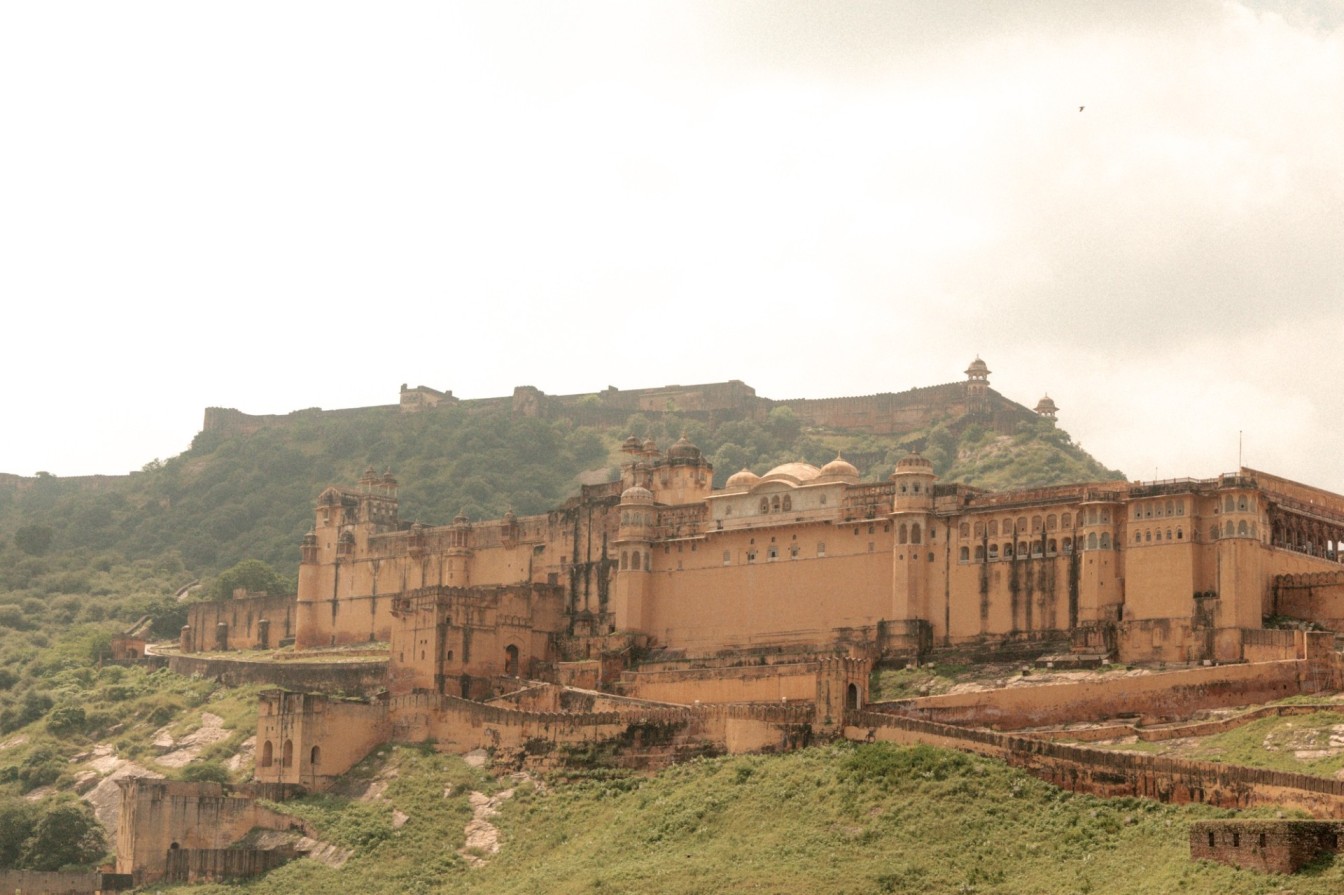 Amber Fort palace complex rising in sandstone tiers along a green hillside in Jaipur Rajasthan India under an overcast sky
