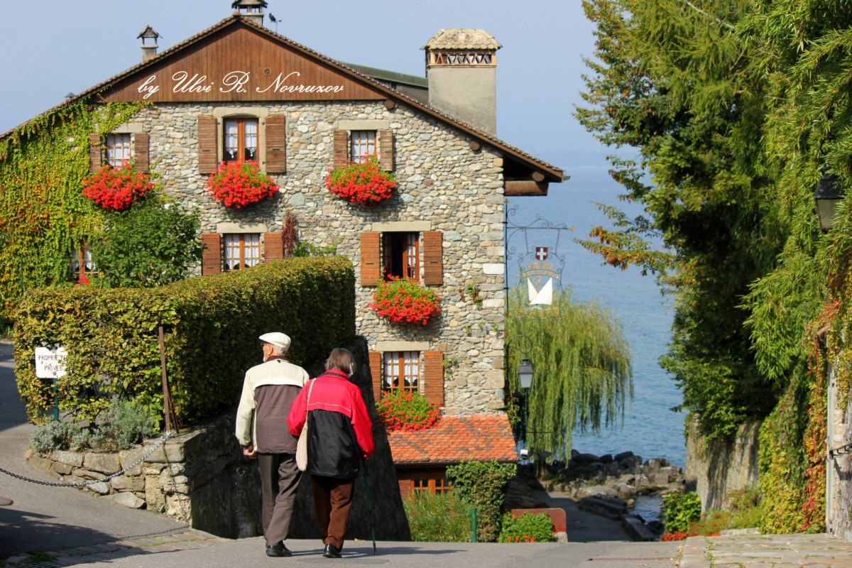 Couple walking through a charming French village with flower-covered stone buildings near Lake Geneva