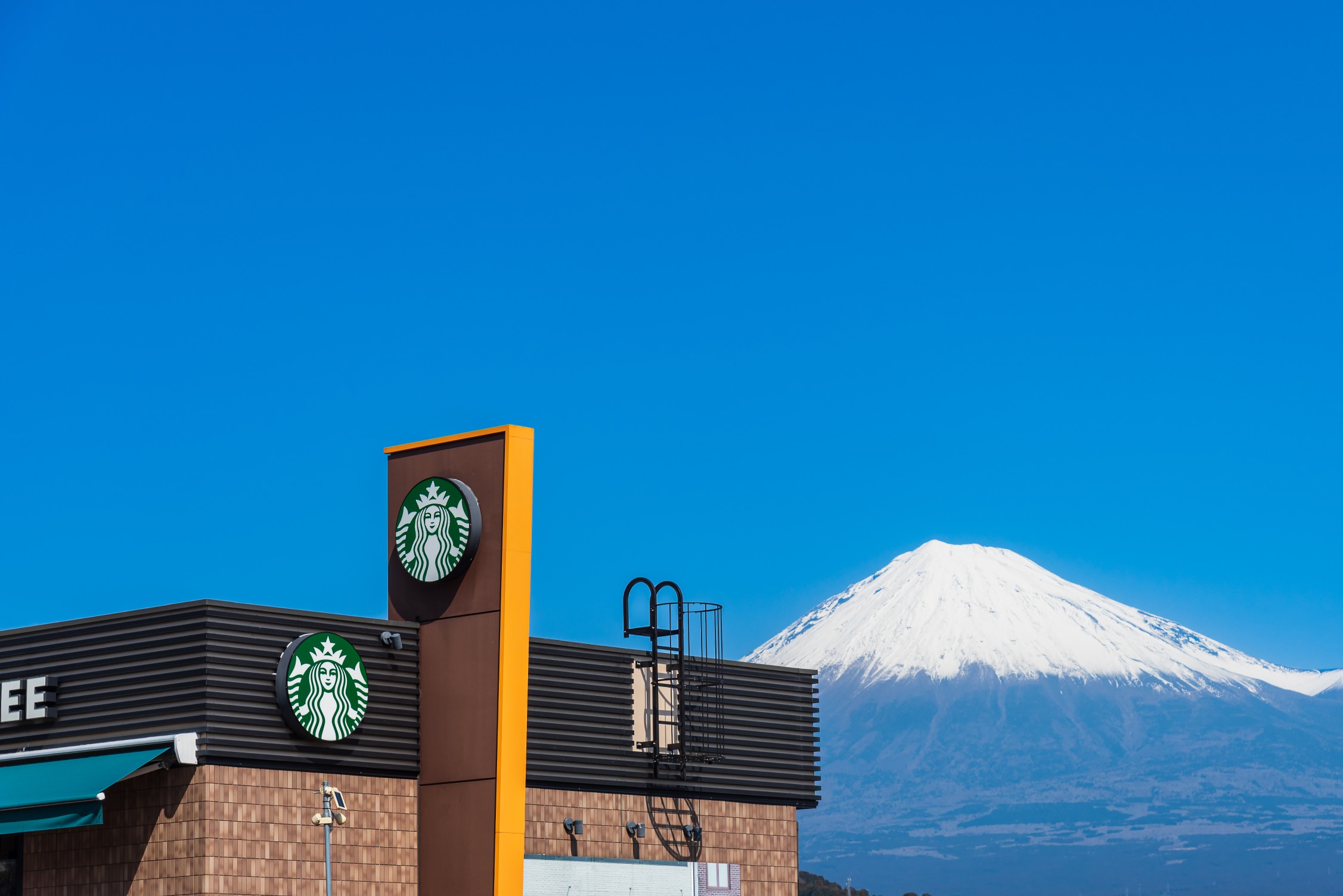 Starbucks coffee shop with its iconic logo situated against the majestic snow capped mount fuji under a clear blue sky. a popular rest stop for tourists in japan. SHIZUOKA, JAPAN - MARCH 1, 2026.