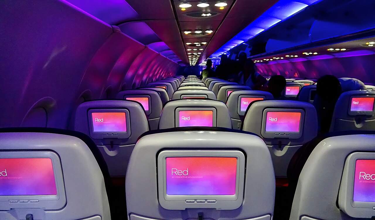 Interior of a Virgin America Airbus A319 cabin, showing the airline’s mood lighting and Red in-flight entertainment screens.
