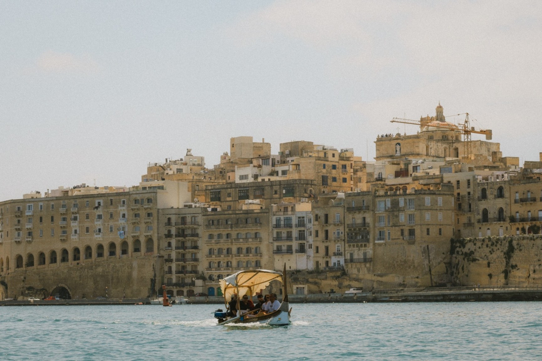 Traditional boat crossing Malta's Grand Harbour with historic waterfront buildings in the background